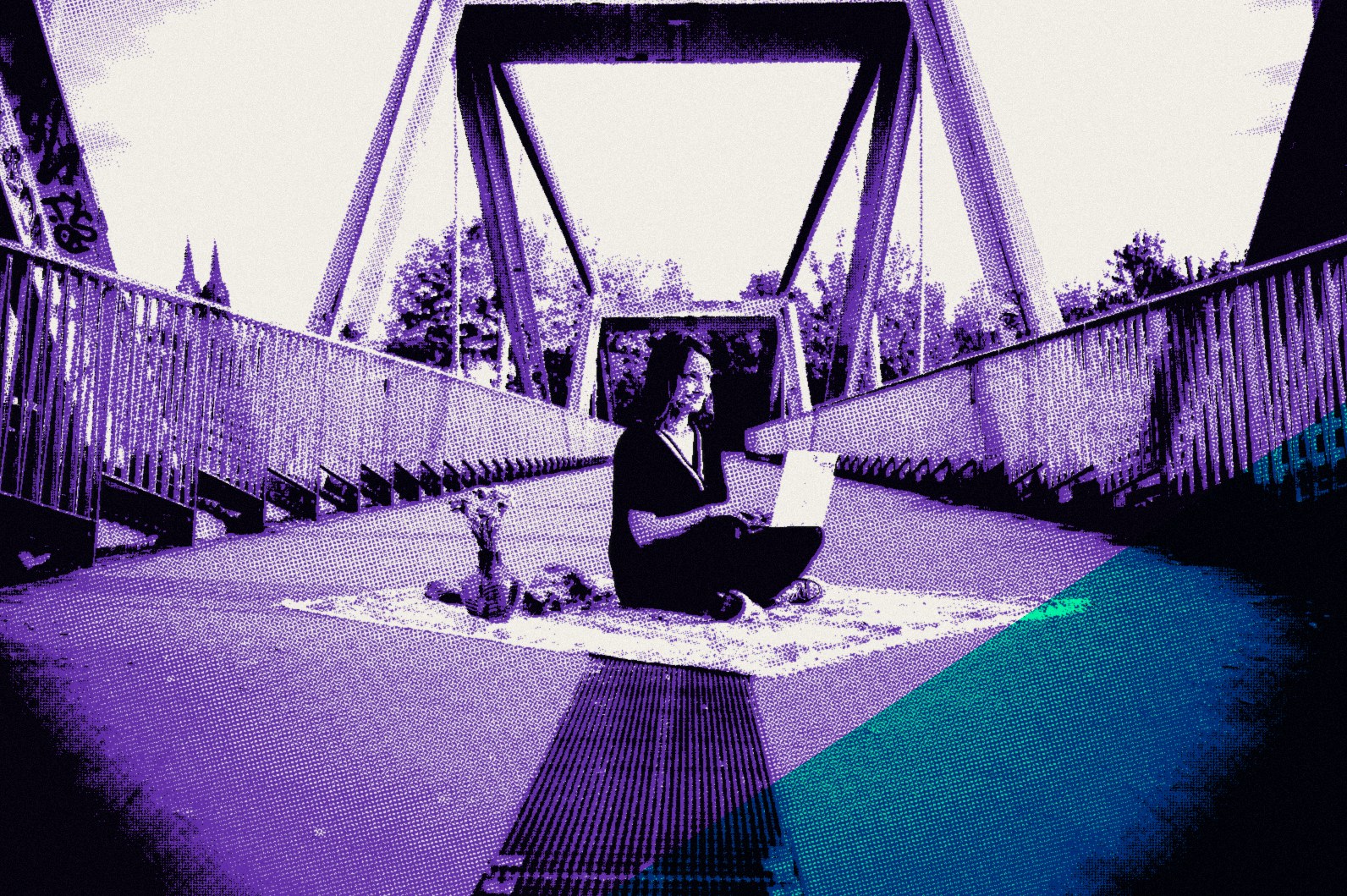 Raphaela Ayriss sitzt mit dem Laptop auf einem Teppich mitten auf einer Brücke in Köln